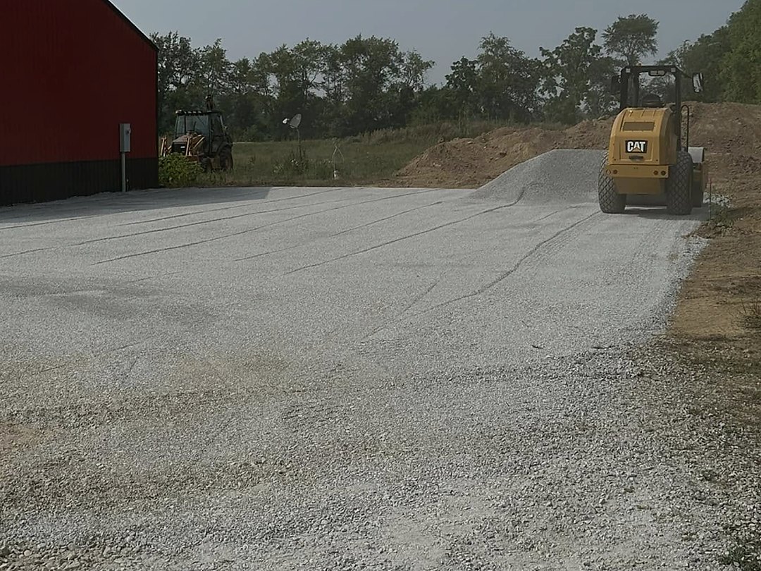 Stone drive running along the side of a dark barn with an excavator working at the end