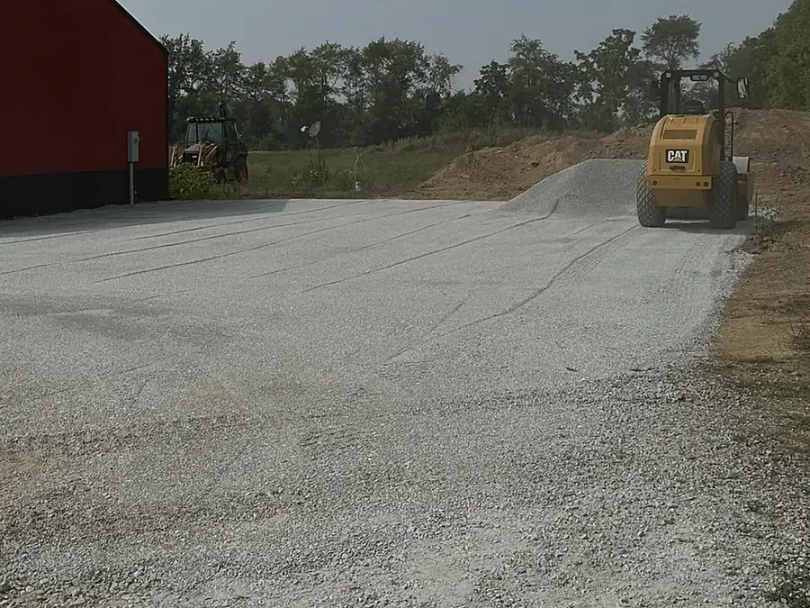 Stone drive running along the side of a dark barn with an excavator working at the end
