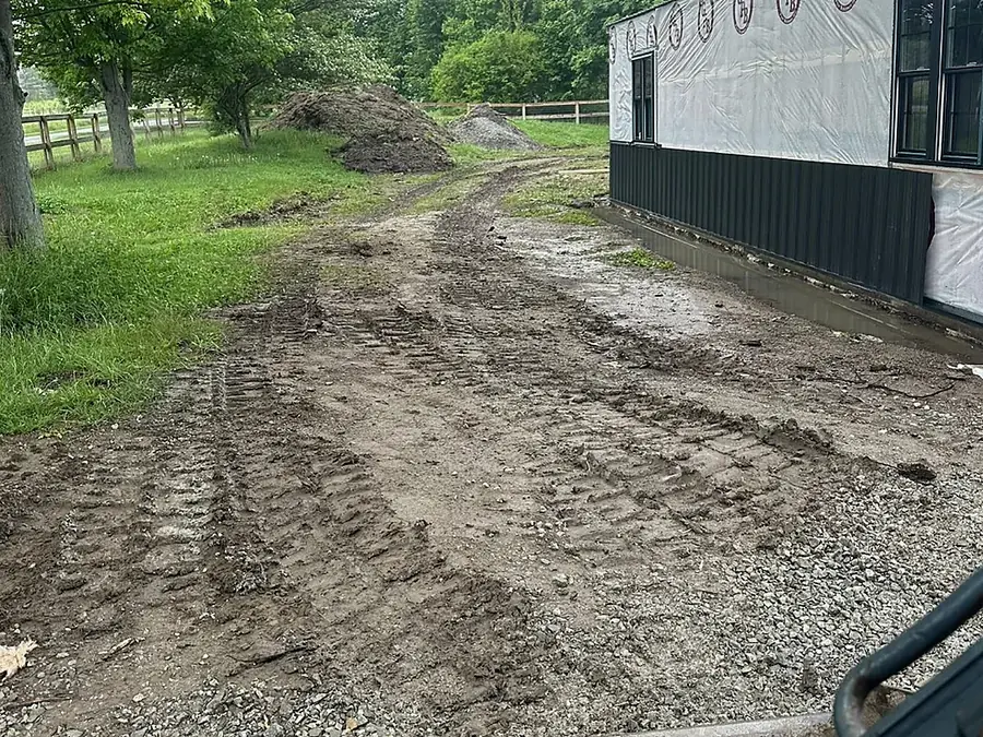 Newly cut driveway base beside a metal building before the final stone lift