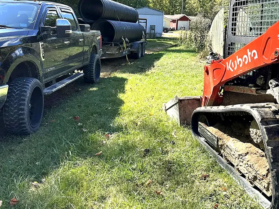 Pickup and trailer with an orange Kubota skid steer loaded, parked on site