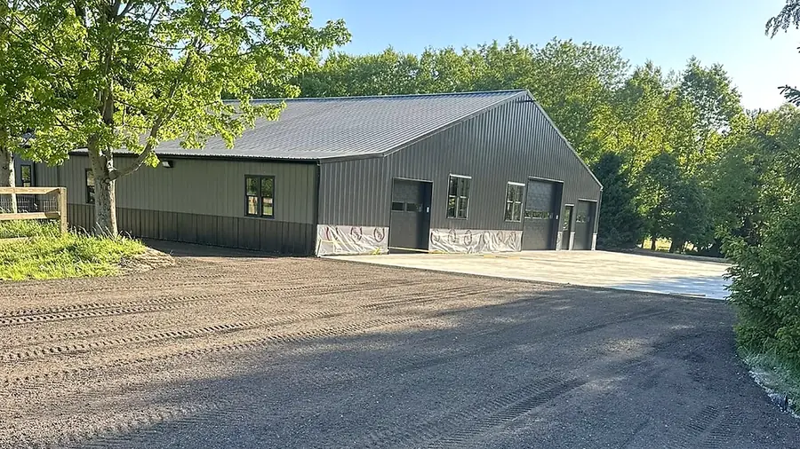 Finished gravel driveway curving up to a metal pole barn under summer trees