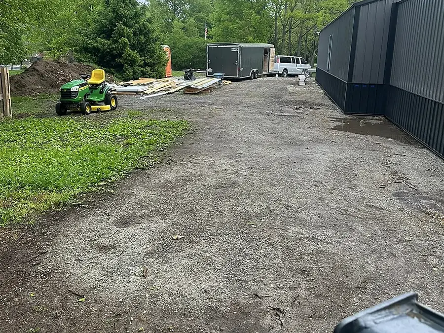 Graded building pad beside a long dark pole barn with equipment on site