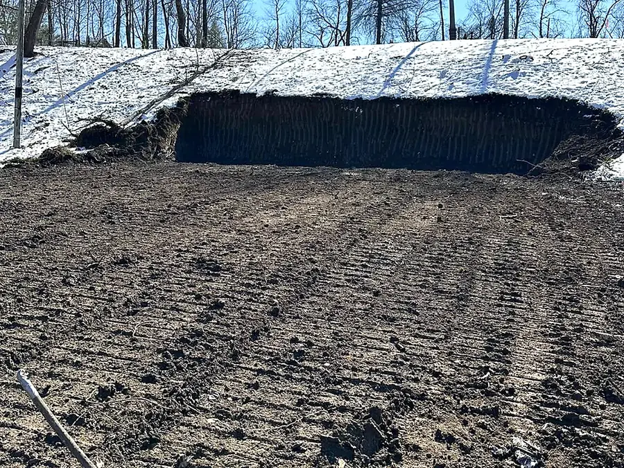 Vertical cut into a snow-covered bank with a levelled working platform graded out below