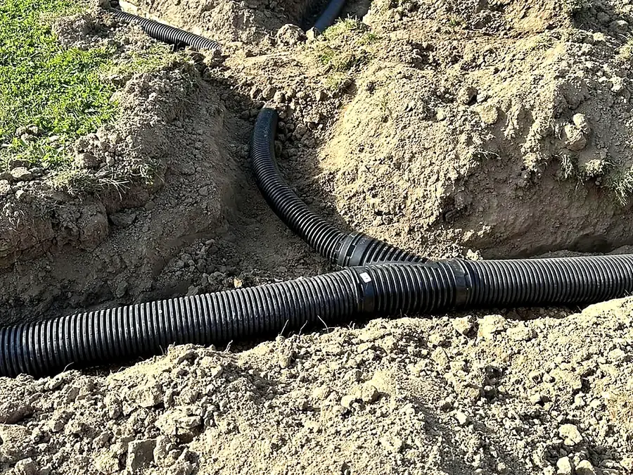 Black corrugated drainage pipe coiled and laid into a shallow trench