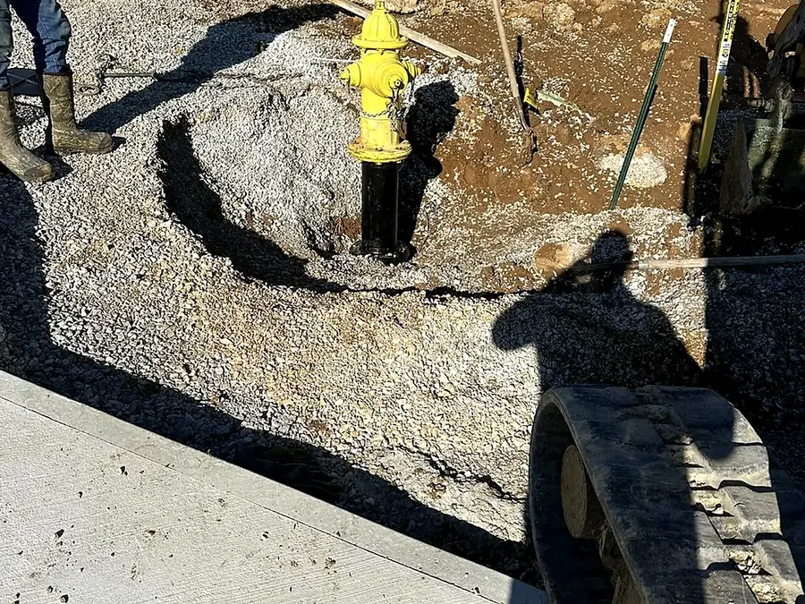 Yellow fire hydrant set in an open excavation with stone bedding around the riser
