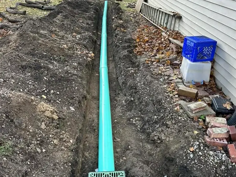 Long green drainage pipe run laid in an open trench beside a house