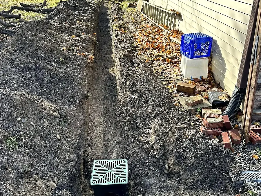 Narrow utility trench dug tight along a house wall with a mini excavator working
