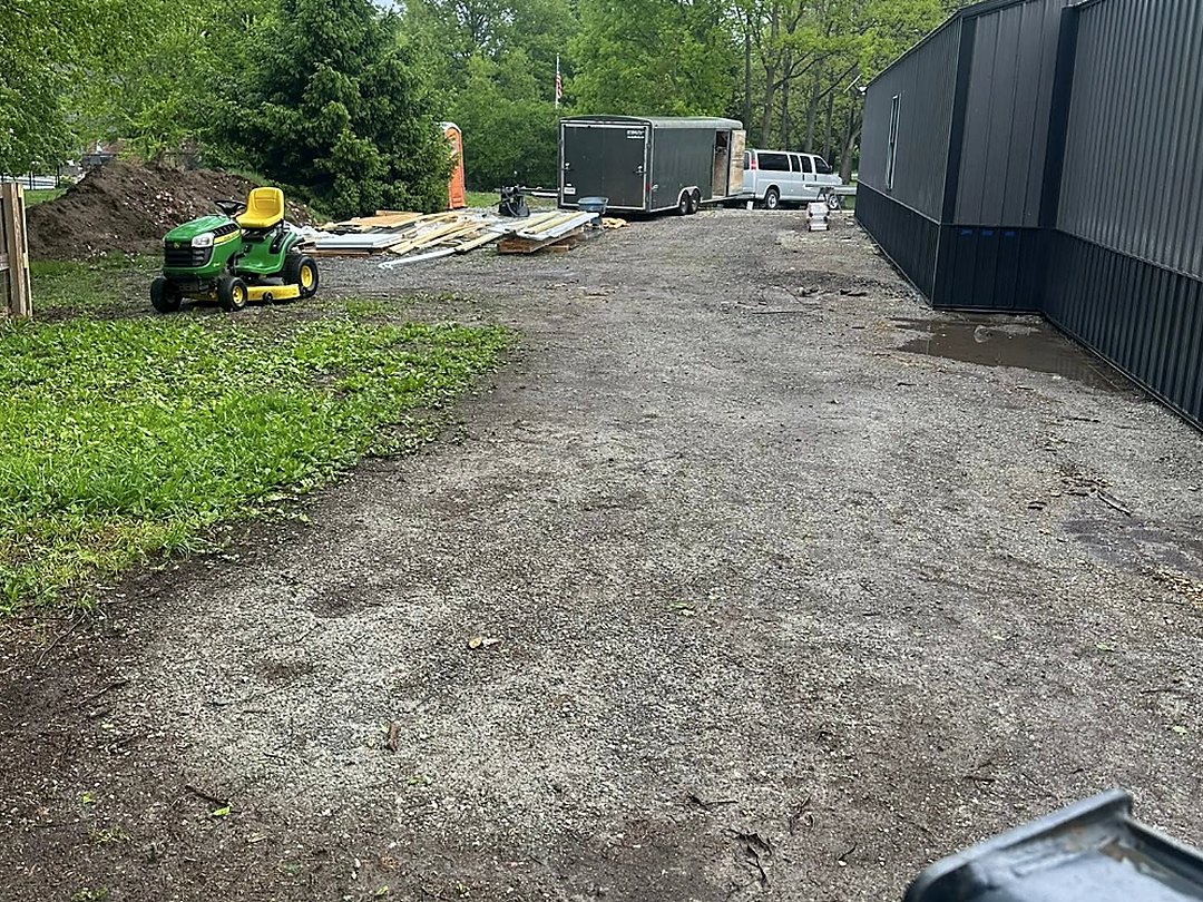 Graded building pad beside a long dark pole barn with equipment on site