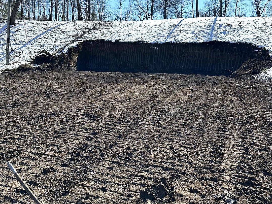 Vertical cut into a snow-covered bank with a levelled working platform graded out below