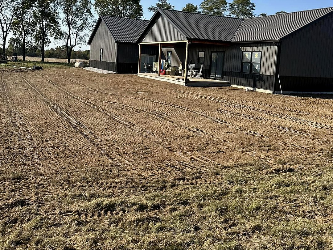 Rough-graded house site with the finished home standing at the back of the lot